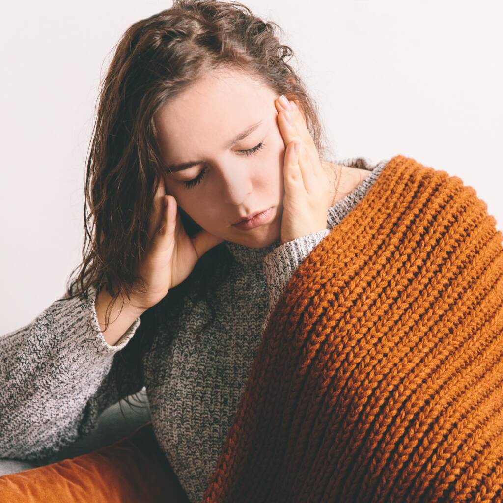 Tired young woman lying on the sofa on white wall background. Headache. Girl holding head